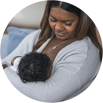 A smiling woman breastfeeding her baby daughter on a couch in her home.